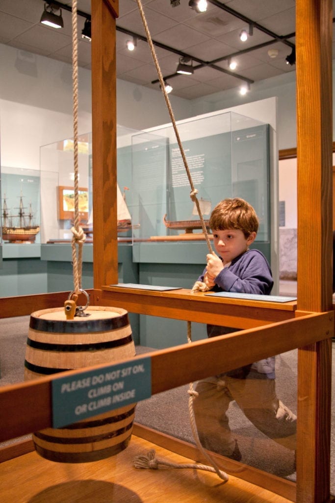 A young boy playing with an interactive display at Ships of the World exhibit at the San Mateo County History Museum