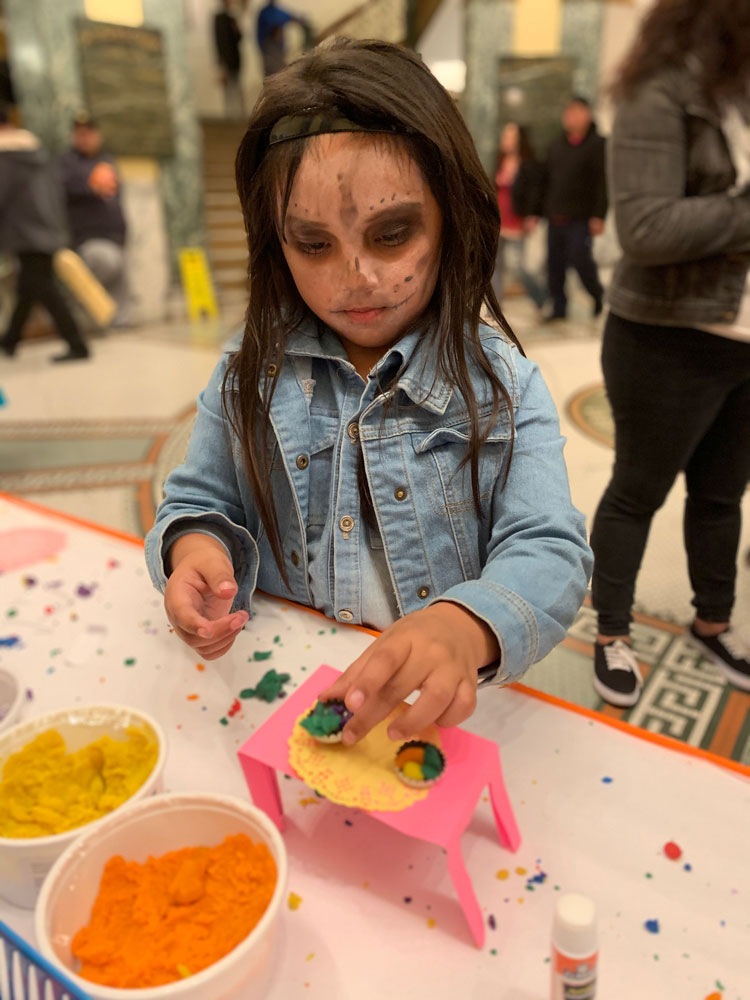 A young girl in Dia de los Muertos face paint works on a craft at the San Mateo County History Museum