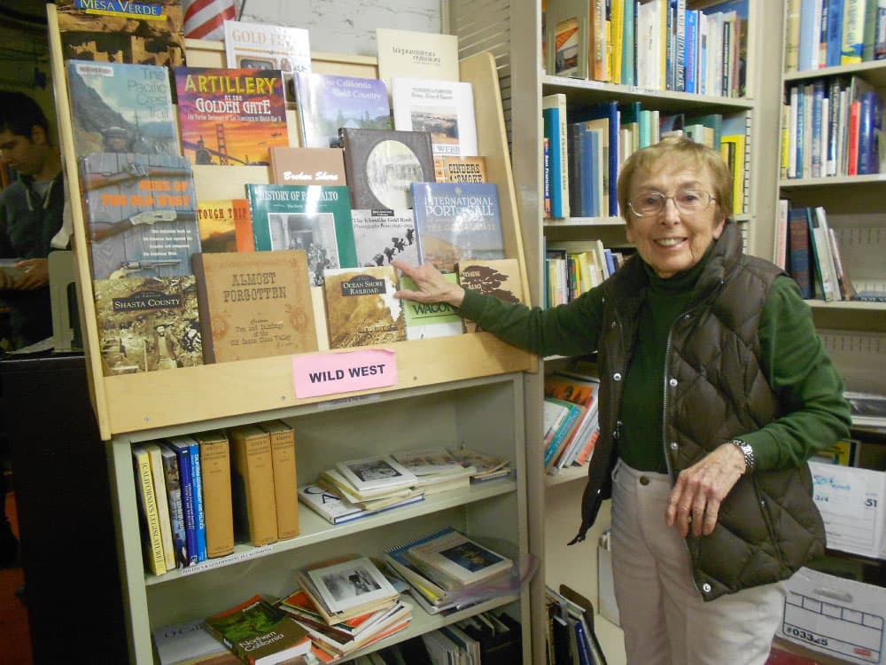 An older female volunteer in front of a book display at Encore Books at the San Mateo County History Museum