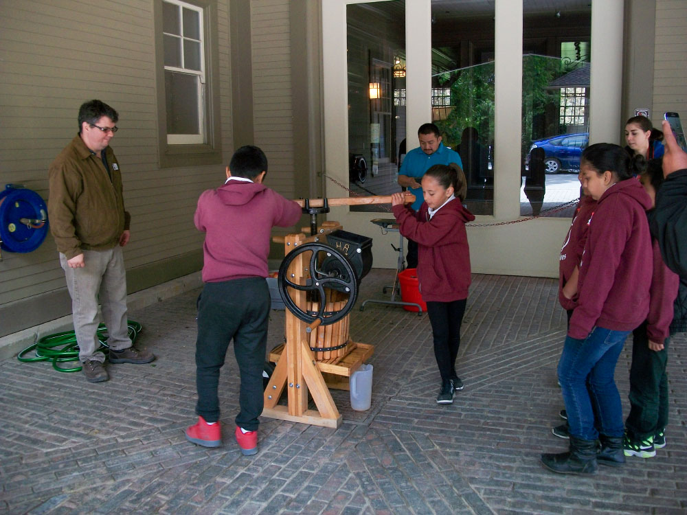 Students at the Folger Stable school program makes apple juice in an old fashioned press