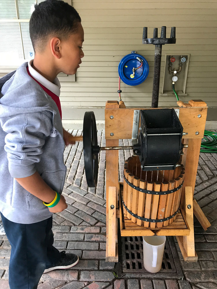 A student at the Folger Stable school program makes apple juice in an old fashioned press