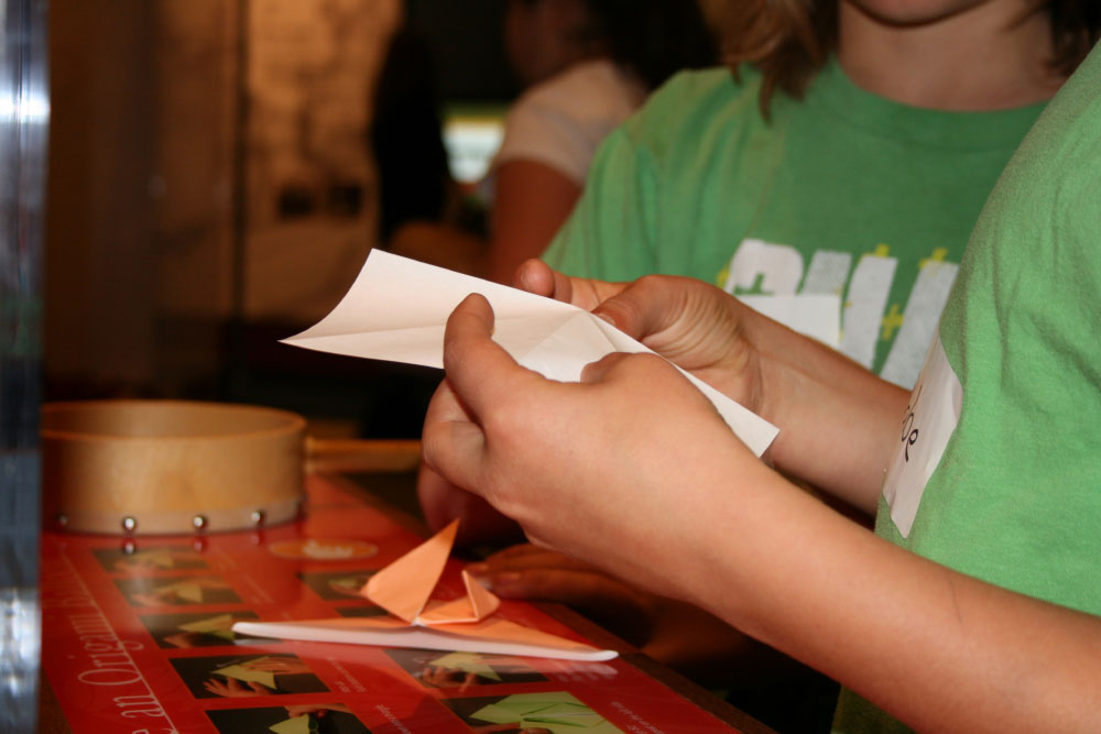 A closeup of a boy folding origami at the Land of Opportunity exhibit at the San Mateo County History Museum