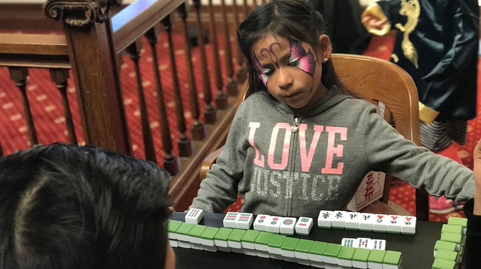 A young girl with butterfly face paint learns mahjong at the lunar new year celebration at the San Mateo County History Museum