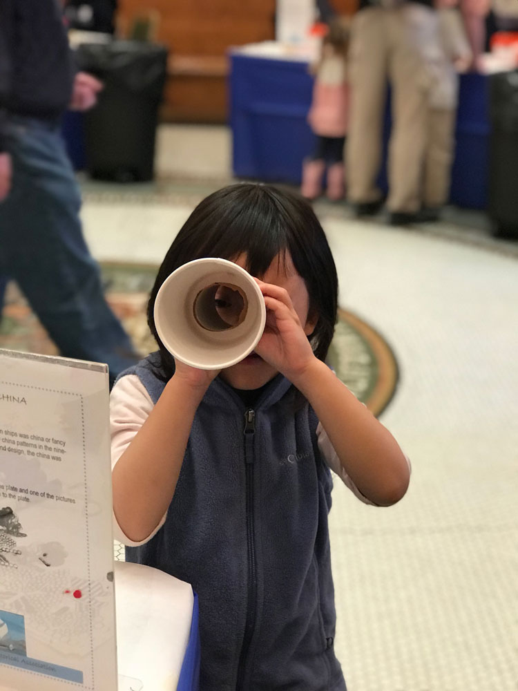 A young girl looks through a makes a handmade telescope craft at Maritime Day at the San Mateo History Museum