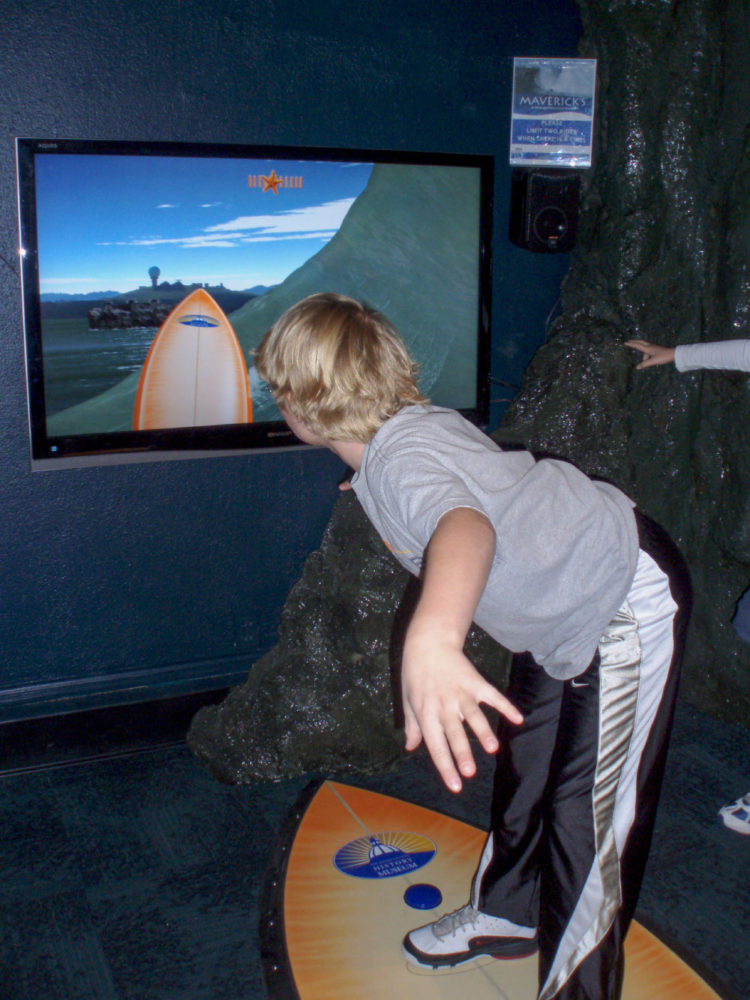 A young boy rides the WaveRider at the Mavericks exhibit at the San Mateo County History Museum