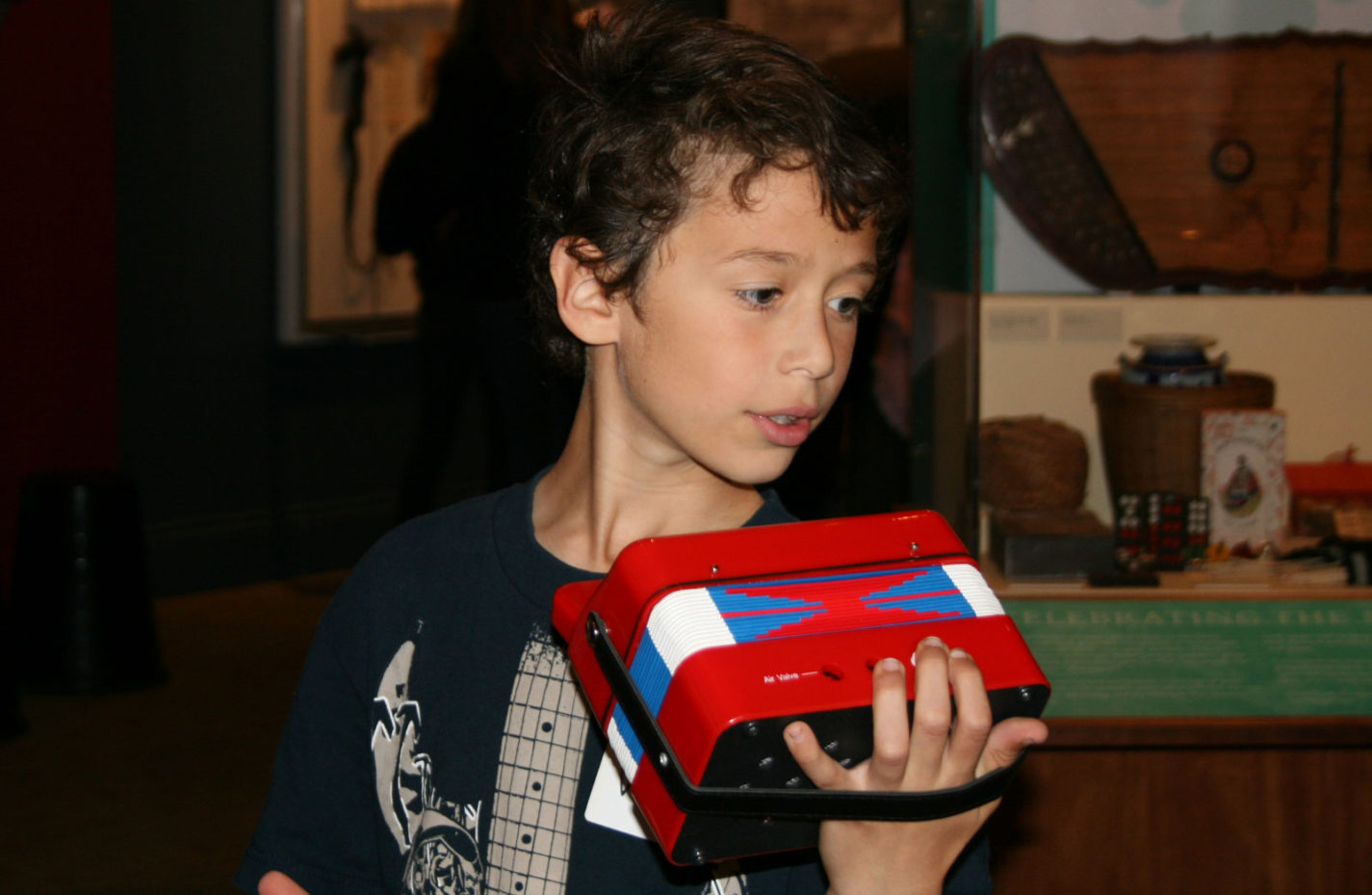 A young student plays a toy accordion at the People from Many Places exhibit at the San Mateo County History Museum