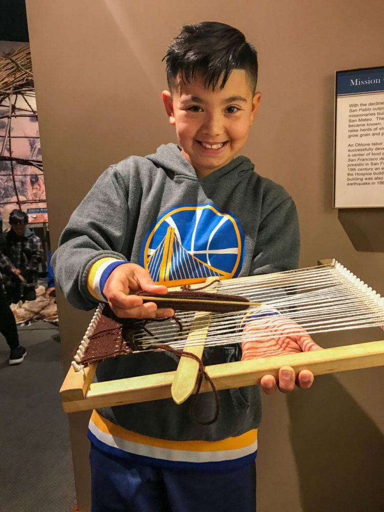 A young student plays with a loom at Providing Plenty school program at the San Mateo County History Museum