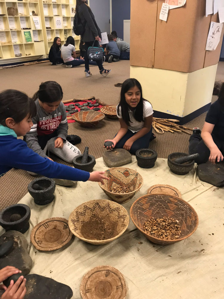 Students use a mortar to ground acorns at Providing Plenty school program at the San Mateo County History Museum