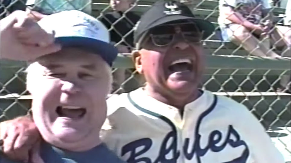 Two older men in baseball uniforms share a laugh at the Old Timers game
