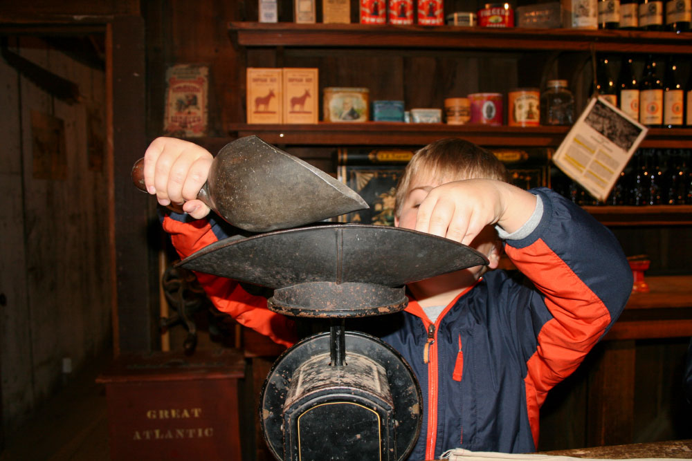 Young boy weighs items on an antique scale at Woodside Store School program