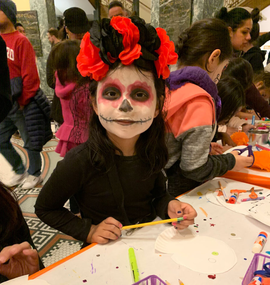 dia-de-los-muertos A young girl in Dia de los Muertos face paint makes a craft at the San Mateo County History Museum