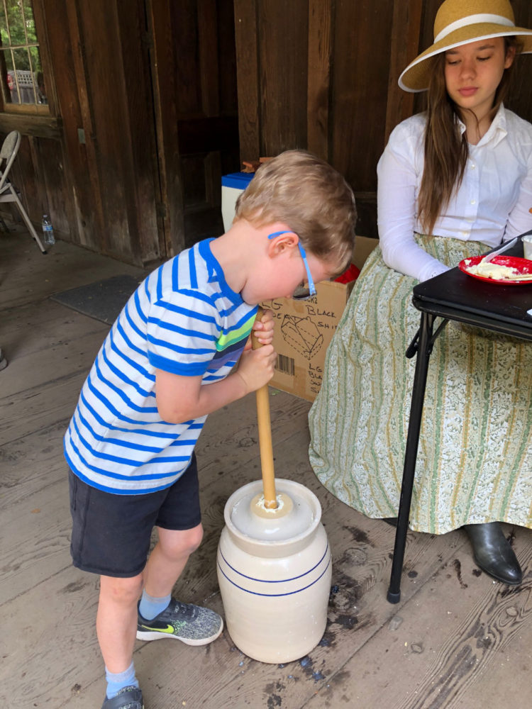 A young boy churns butter at the Old Woodside Store Day