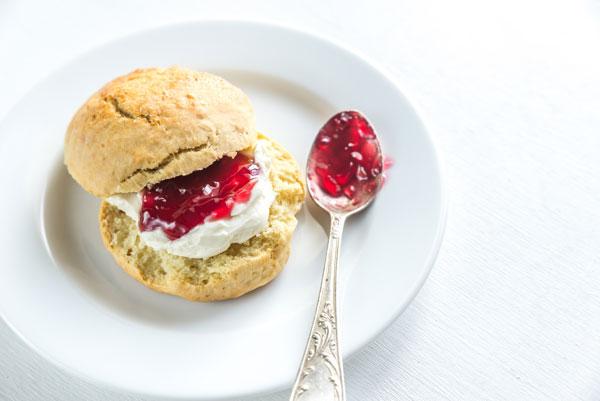 Scone with cream and cherry jam on a spoon on a plate