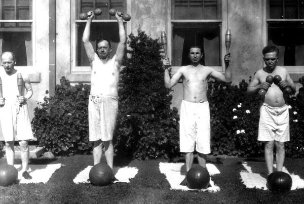 Four men participate in physical exercise with wood weights in the 1950s