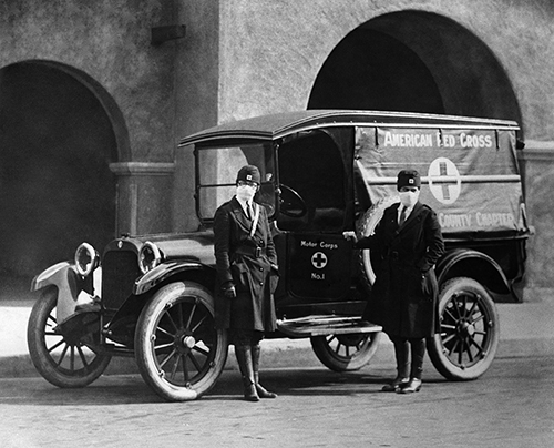 Two women in masks standing in front of an early ambulance