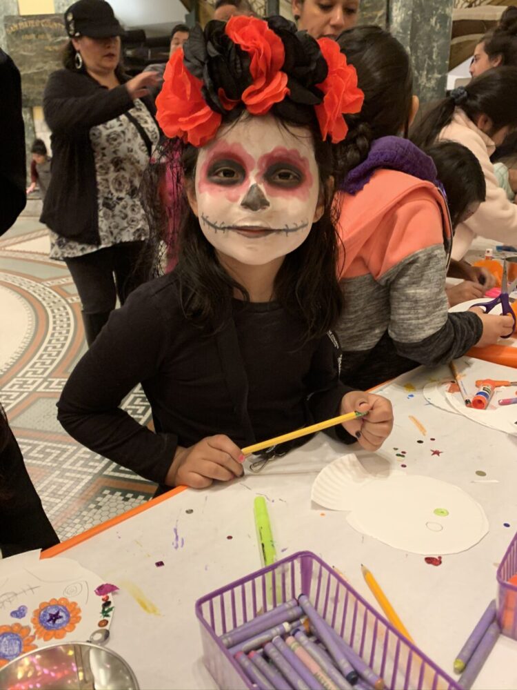 Young girl dressed as la catrina posing at a craft table.