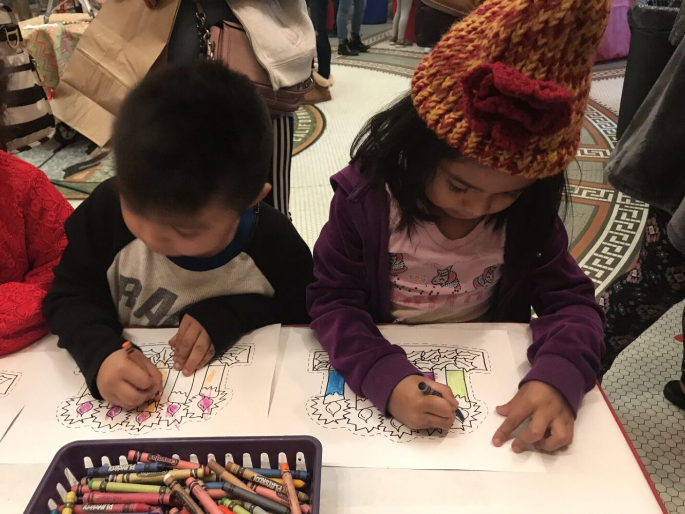 Two young children color in a holiday craft.